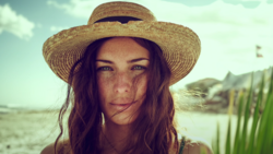 Woman wearing a straw hat looking directly at camera outdoors.