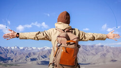 Hiker with arms spread wide standing in mountainous desert landscape under clear blue sky.