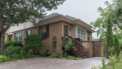 Brick residential home with ivy-covered entrance and wooden deck surrounded by mature trees.