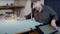 Man in dark shirt demonstrating color swatches on a blue surface with tablet displaying matching palette.