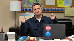 Man giving double thumbs up while sitting at a desk with a laptop.