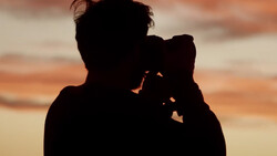 Silhouetted figure holding a child against a golden sunset sky.