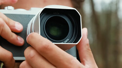 Close-up of hands holding a white compact camera with a dark lens element visible.