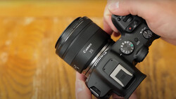 Hands holding a Canon mirrorless camera with a 35mm lens against a warm, textured yellow background.