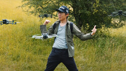 Drone operator in a grassy field wearing a cap and jacket, launching multiple drones.
