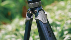 Close-up of a tripod head with ball joint and adjustment knobs against a blurred green outdoor background.