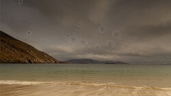 Coastal landscape with turquoise water, sandy beach, and rocky headland under dramatic storm clouds.