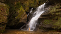 Multi-tiered waterfall cascading over moss-covered rocks into a shallow pool.