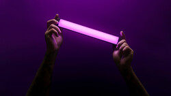 Two hands holding a glowing pink neon tube against a deep purple background.