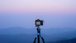 DSLR camera mounted on blue tripod against layered mountain silhouettes at twilight.