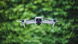 Compact quadcopter drone hovering against blurred green foliage background.