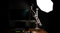 Professional studio setup with monitor, articulating desk lamp, and softbox lighting on dark background.