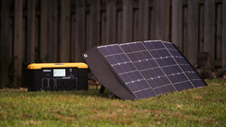 Portable power station with solar panel array on grass against wooden fence backdrop.