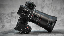 Mirrorless camera with telephoto lens mounted on motorized gimbal head against textured gray backdrop.