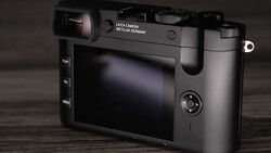 Leica camera with rear LCD screen displayed at three-quarter angle on wooden surface.