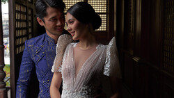 Couple in formal traditional attire standing together indoors with warm architectural lighting.