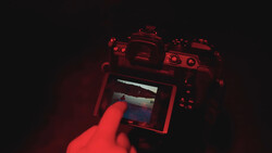 Photographer's hand holding a mirrorless camera with LCD screen visible in red-tinted lighting.