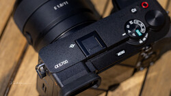 Sony α5700 mirrorless camera with attached lens on wooden surface, showing top plate controls and mode dial.