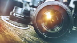 Camera lens with golden light flare and optical elements visible through glass.