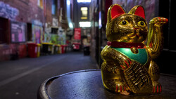 Golden beckoning cat figurine with red ears and green bib on a blurred nighttime street.