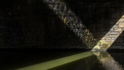 Sunlight streaming through a narrow passageway between dark stone walls and still green water below.