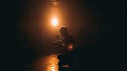 Silhouetted figure holding a camera in a dark corridor, backlit by warm golden light.