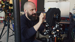 Cinematographer adjusting a large format cinema camera mounted on a rig in a studio setting.
