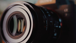 Close-up of a camera lens with focus on the front element and focus ring, shot at shallow depth of field.