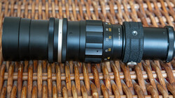 Vintage telephoto lens disassembled showing internal glass elements and mechanical components on woven surface.