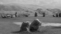 Two weathered standing stones in foreground with row of distant megaliths and rolling hills in black and white.