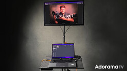 Monitor on adjustable stand displaying portrait of person with arms outstretched, laptop below showing editing interface.