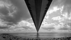 Long bridge viewed from underneath, stretching toward horizon with dramatic cloudy sky.