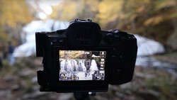 Camera on tripod displaying waterfall footage on LCD screen with blurred background.