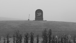 Gravestone with bird relief silhouetted against overcast sky on a hillside.