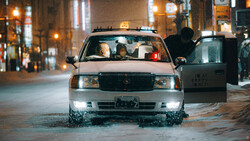 Taxi cab driving through flooded urban street at night with city lights in background.