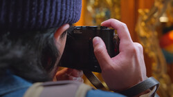 Photographer's hands holding a compact camera in portrait orientation outdoors during golden hour.