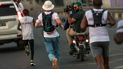 Urban street runners moving past a motorcyclist during daytime in a busy city setting.