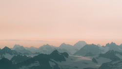 Layered mountain silhouettes in mist under a peachy dawn sky.