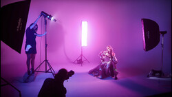 Professional studio photography shoot with magenta-pink lighting and multiple light sources positioning a seated subject.
