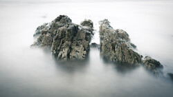 Two jagged rock peaks emerging from dense fog and mist in a mountainous landscape.