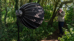 Large black parabolic softbox suspended in a forest setting during outdoor photography shoot.
