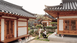 Traditional East Asian courtyard with red wooden buildings, curved tile roofs, and manicured garden with stone pathways.