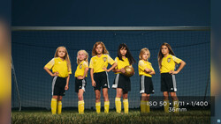Six young soccer players in yellow jerseys and black shorts stand in a line in front of a goal net.