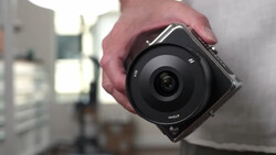 Person holding a compact mirrorless camera with a wide-angle lens in an interior space with natural window light.