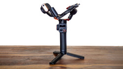 Three-axis motorized gimbal with camera mounted on wooden surface and black tripod base.