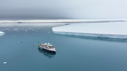 Expedition cruise ship navigating through icy Arctic waters surrounded by white ice floes and a massive ice shelf.