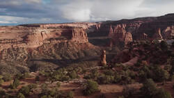 Desert canyon landscape with layered red rock formations and sparse vegetation in valley.