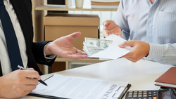 Two people exchange cash and documents at a desk during a business transaction.