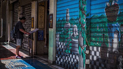 Person in dark shirt standing at blue metal storefront gate with painted library mural depicting books and architecture.