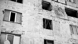 Abandoned concrete apartment building with boarded windows and crumbling facade.